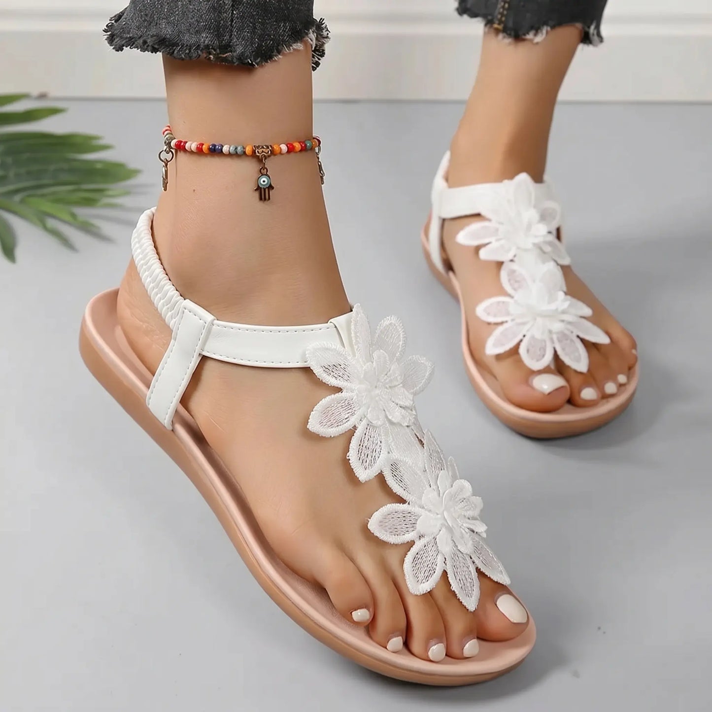 White Aethel bohemian flat thong sandals featuring intricate layered floral appliques and a comfortable elasticated slingback strap, shown on a model's foot with a grey background.