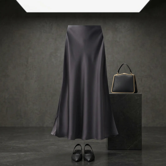 Elegant black satin high-waisted midi skirt with an A-line mermaid drape, styled in a dark studio setting with a coordinating handbag and shoes.