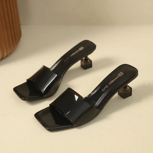 Black square toe slip-on mule sandals featuring a single wide PU strap and a clear transparent geometric block heel.