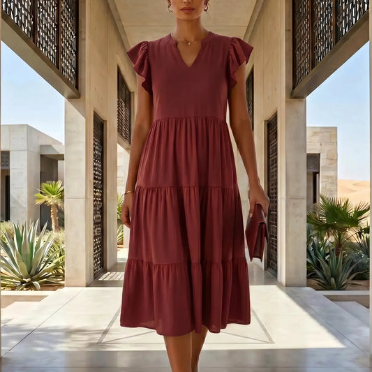 Bordeaux Wine Torvun tiered midi dress featuring a V-neck and ruffle cap sleeves, worn by a woman walking through an elegant architectural setting.