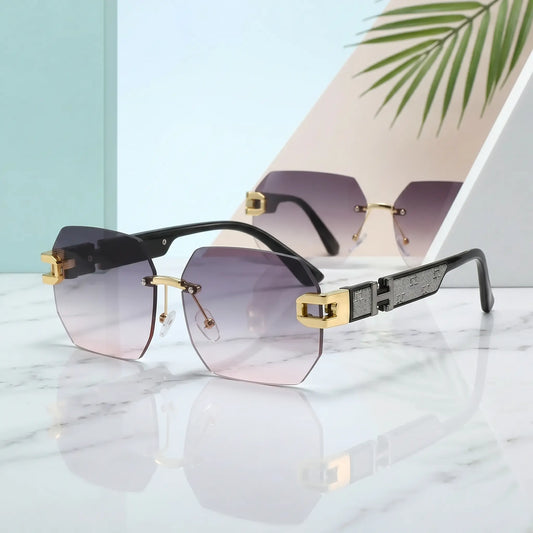 Rimless geometric sunglasses featuring gradient smoky grey to pink lenses and polished gold-tone accents at the temples and bridge, displayed on a marble surface with studio background elements.