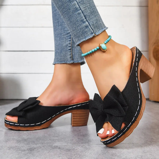 Black Kaelen women's slip-on sandals featuring a textured fabric bow, fish-mouth peep-toe, and a 7cm wood-grain block heel, styled with blue denim and an anklet.