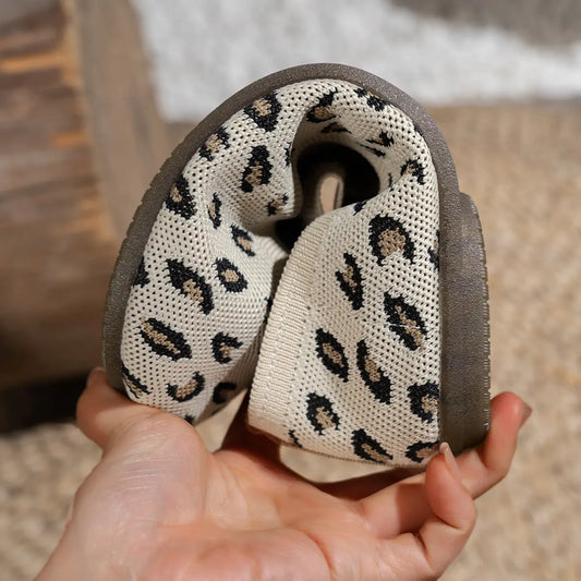 Close-up of Kaelen women's knit ballet flats showcasing the creamy off-white base with black and brown leopard print pattern and a flexible dark rubber sole held by hand.