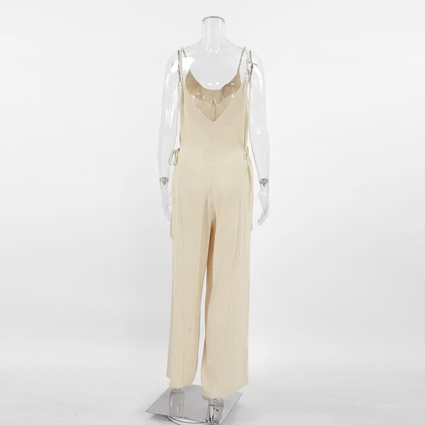 Back view of a Kaelum beige linen-blend wide-leg jumpsuit featuring spaghetti straps, a low V-neckline, and adjustable side ties. The relaxed silhouette has full-length, straight-leg pants and a matte, textured finish.