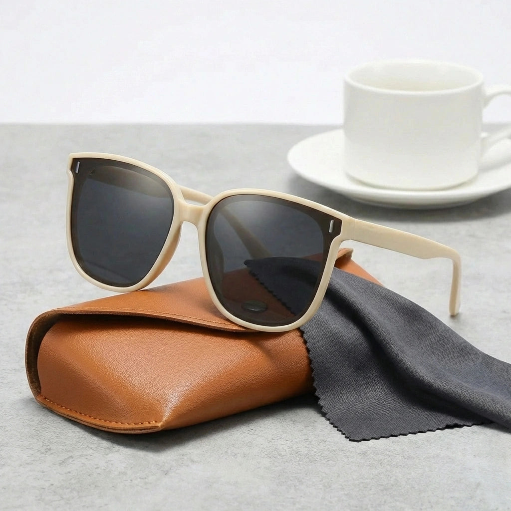 KAEON oversized square sunglasses in sandstone beige resting on a leather case, showing the chunky architectural frame and dark UV400 lenses.
