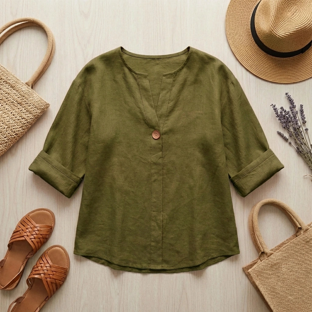 Luvana olive green linen blend blouse in a flat-lay arrangement with summer accessories including a straw hat, sandals, and a tote bag.
