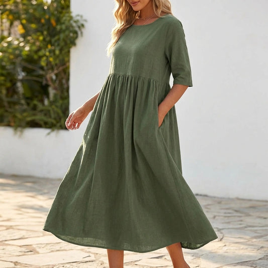 Luvia cotton linen midi dress in sage green with relaxed fit, elbow-length sleeves, and side pockets, worn by a model outdoors.
