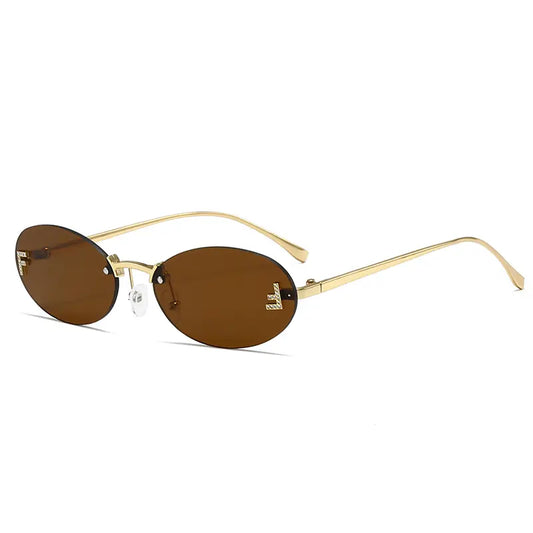 Lyraxa oval rimless sunglasses featuring a polished gold metal frame and warm brown tinted lenses, with decorative jeweled letter embellishments on the temples. These elegant sunglasses offer UV400 protection and adjustable nose pads for a comfortable fit.