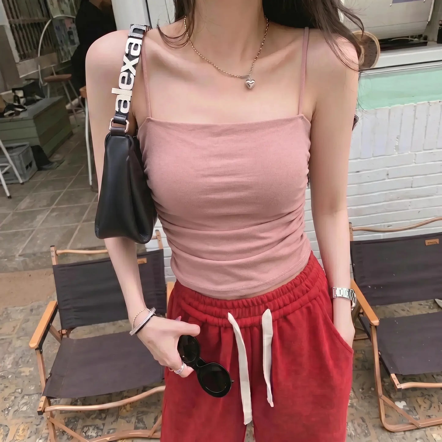 Model wearing a Soft Rose ruched camisole top with spaghetti straps, showcasing its slim fit and textured front, in an outdoor lifestyle setting.