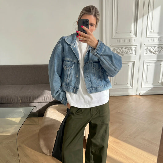 Woman wearing high-rise, olive green wide-leg utility trousers with front patch pockets, styled casually with a denim jacket and white t-shirt in a modern interior.