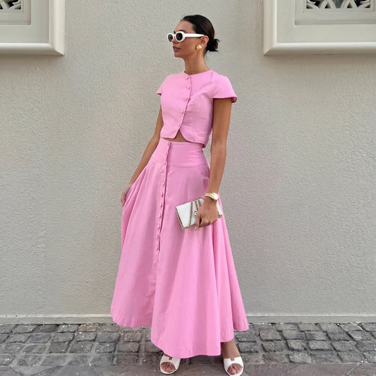 Woman wearing a vibrant pink cotton two-piece set featuring a cropped button-up top with cap sleeves and a flowing A-line midi skirt with a full button-down front.