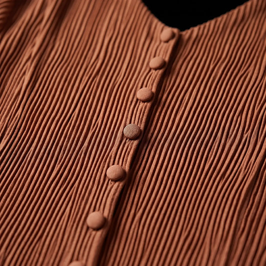 Close-up of the Zethrin pleated midi dress in Terracotta Red, highlighting the finely textured micro-pleats and matching fabric-covered buttons along the V-neckline placket.