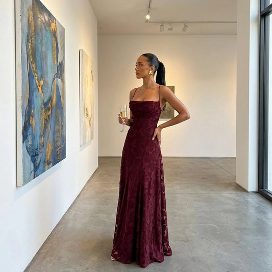 Veloura burgundy jacquard maxi dress with cowl neckline and textured floral pattern, modeled in an elegant art gallery setting.