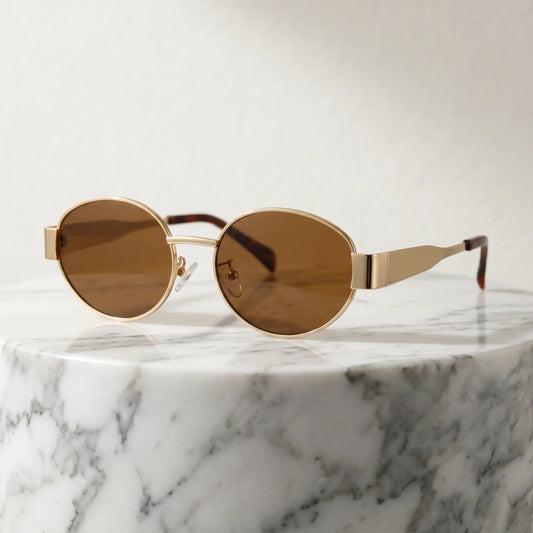 Gold-toned vintage oval metal frame sunglasses with brown tinted lenses and tortoiseshell temple tips, presented on a marble pedestal.