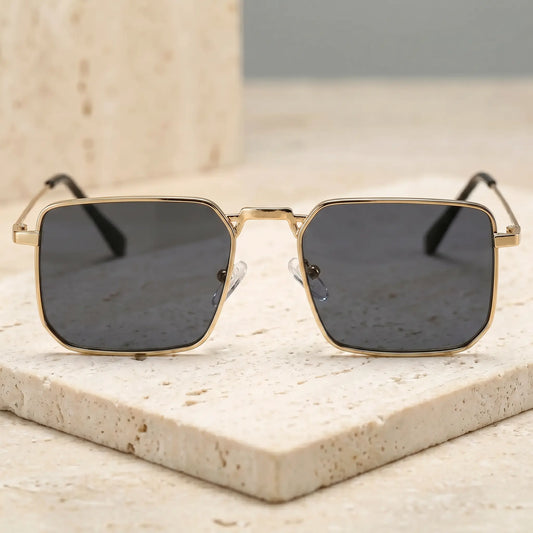 Tavren vintage square sunglasses featuring gilded gold metal frames and dark slate grey lenses, viewed from the front on a textured studio surface.