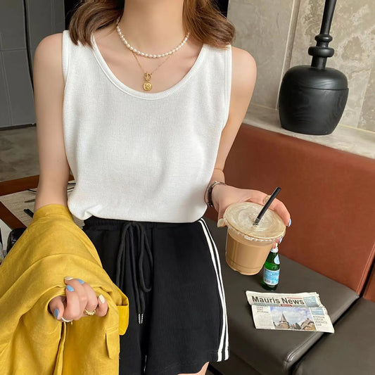 Female model wearing a white Koryx waffle knit sleeveless camisole with a scoop neck and wide straps, styled in a casual lifestyle setting, holding an iced coffee.