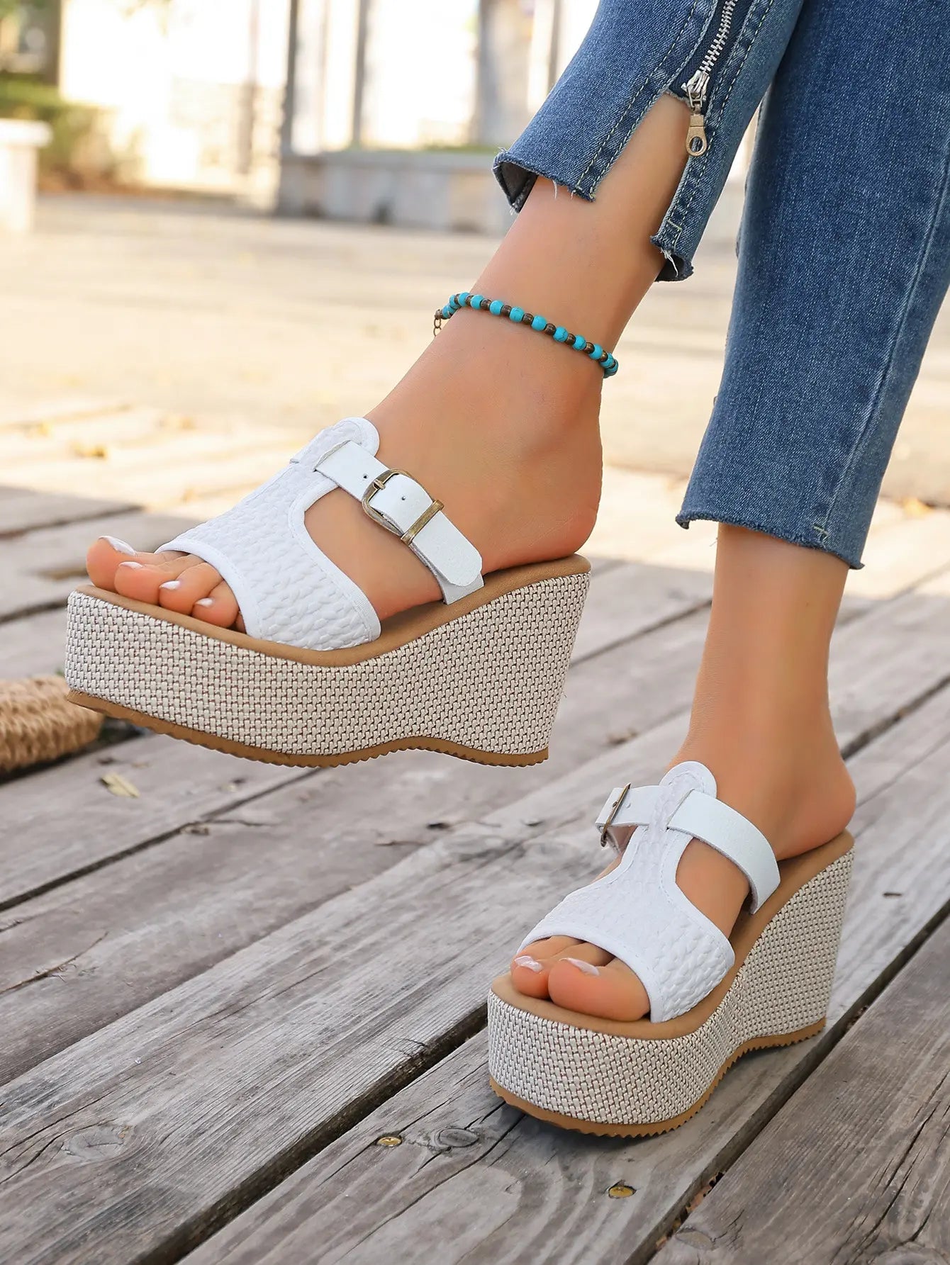 Women's white woven platform espadrille wedge sandals with T-strap and buckle closure, styled with denim jeans and a turquoise anklet.