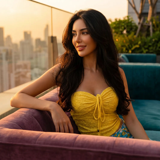 Model wears a vibrant yellow textured strapless ruched top with drawstring, seated on a purple couch during sunset.