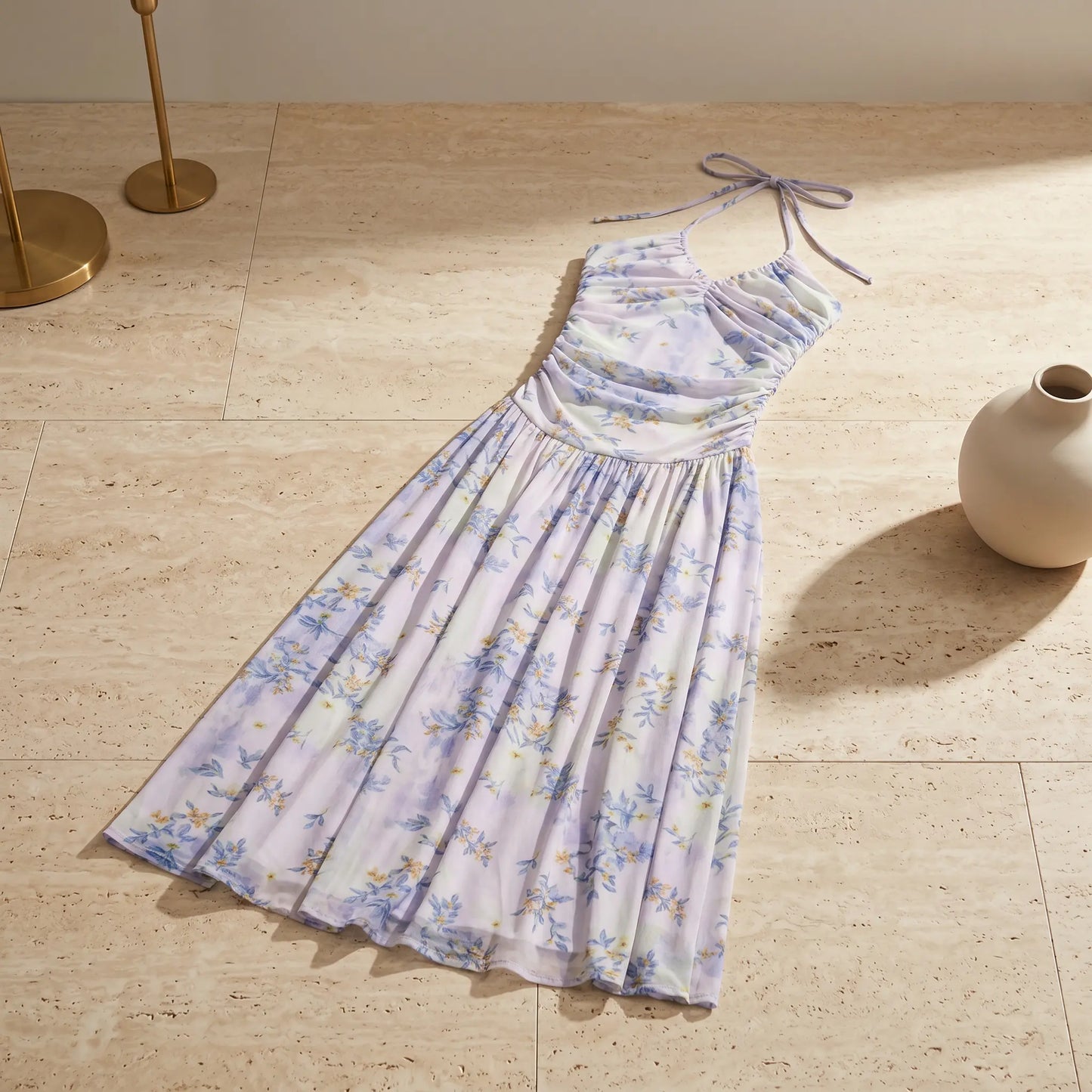 Zevrak lilac floral mesh ruched maxi dress laid flat on beige tiles, showcasing the halter neck ties and blue and yellow flower pattern. The heavily ruched bodice and flowing A-line skirt are visible.