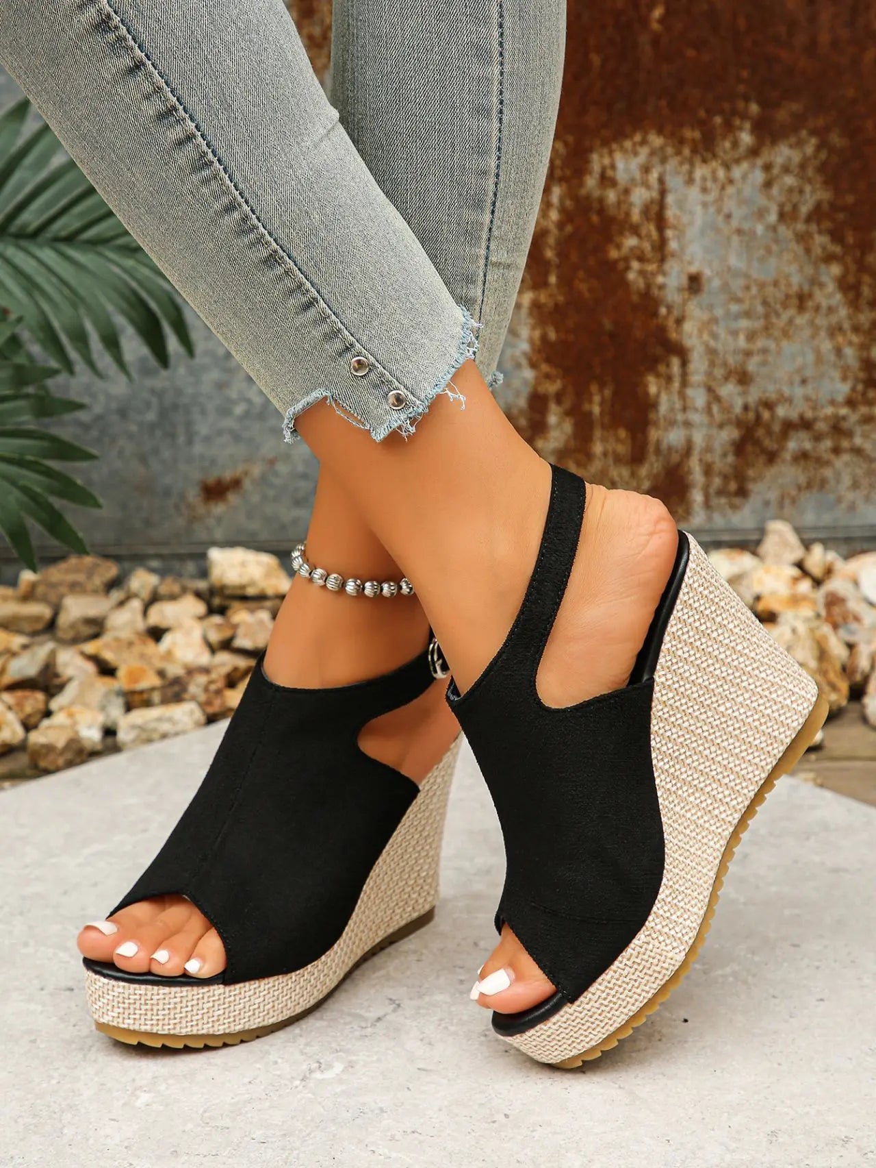 Black peep-toe espadrille wedge sandals with jute-wrapped heels, worn by a model with distressed jeans and an ankle bracelet. Focus on the bohemian chic style and comfortable height.