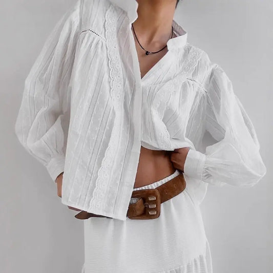 A white jacquard cotton blouse with delicate floral lace trim and voluminous bishop sleeves is styled by a model with a brown belt and necklace.