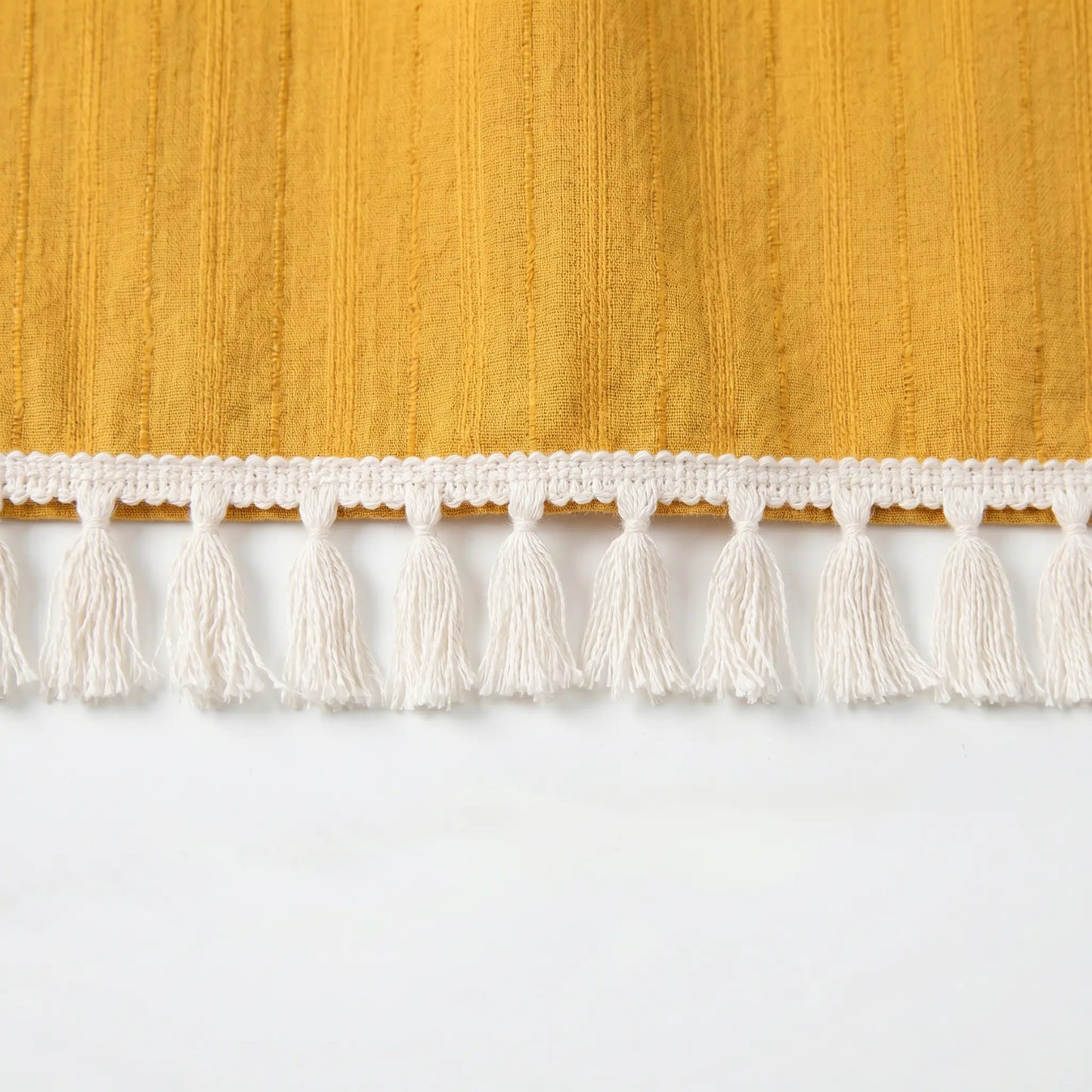 Detail of the Zovith golden-mustard Bohemian Maxi Dress, highlighting the textured vertical stripe fabric and exquisite cream tassel fringe hem.