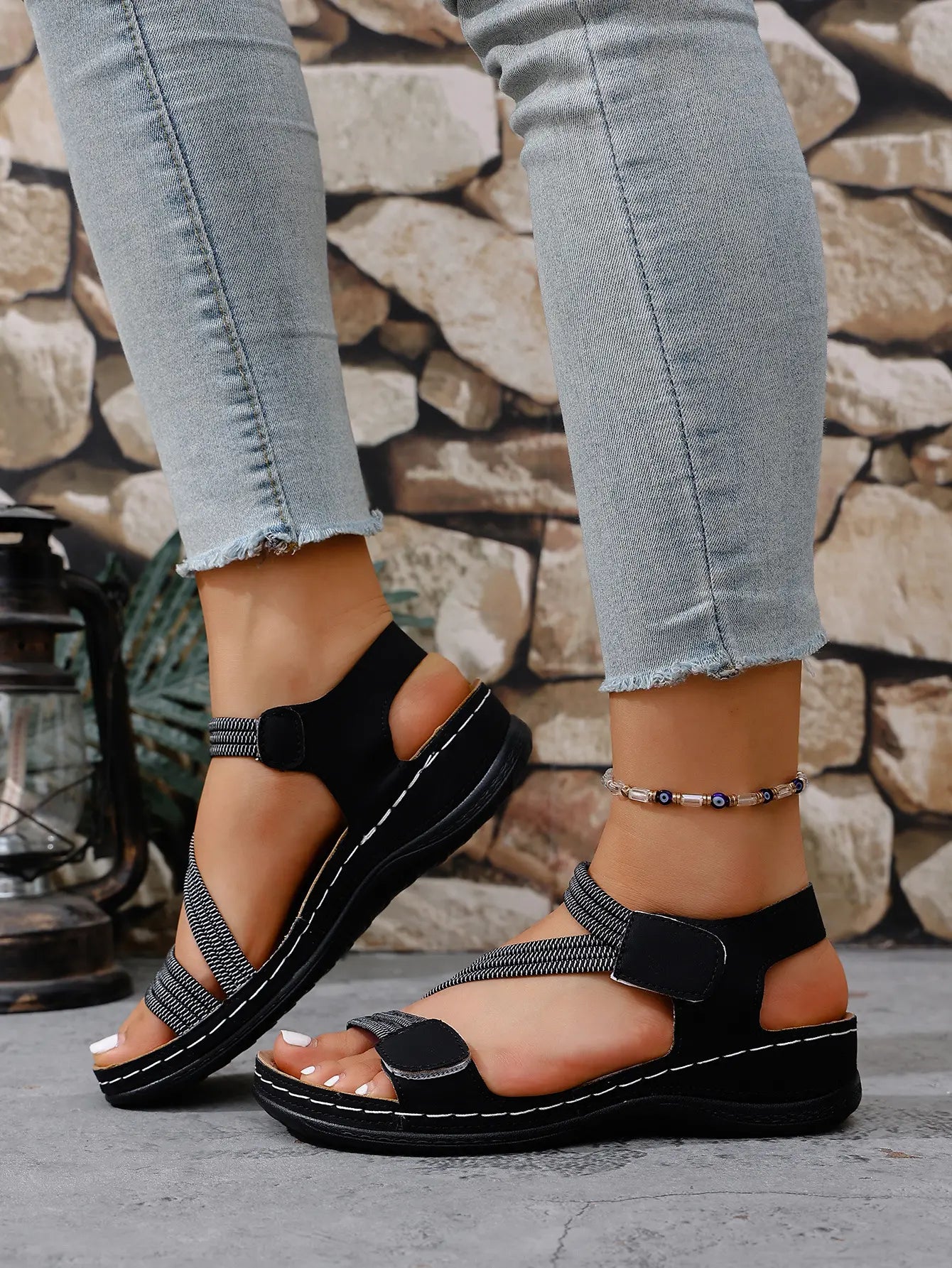 Close-up of women's black Zykla comfort sport sandals with elastic criss-cross straps and white stitching, styled with light-wash denim jeans.