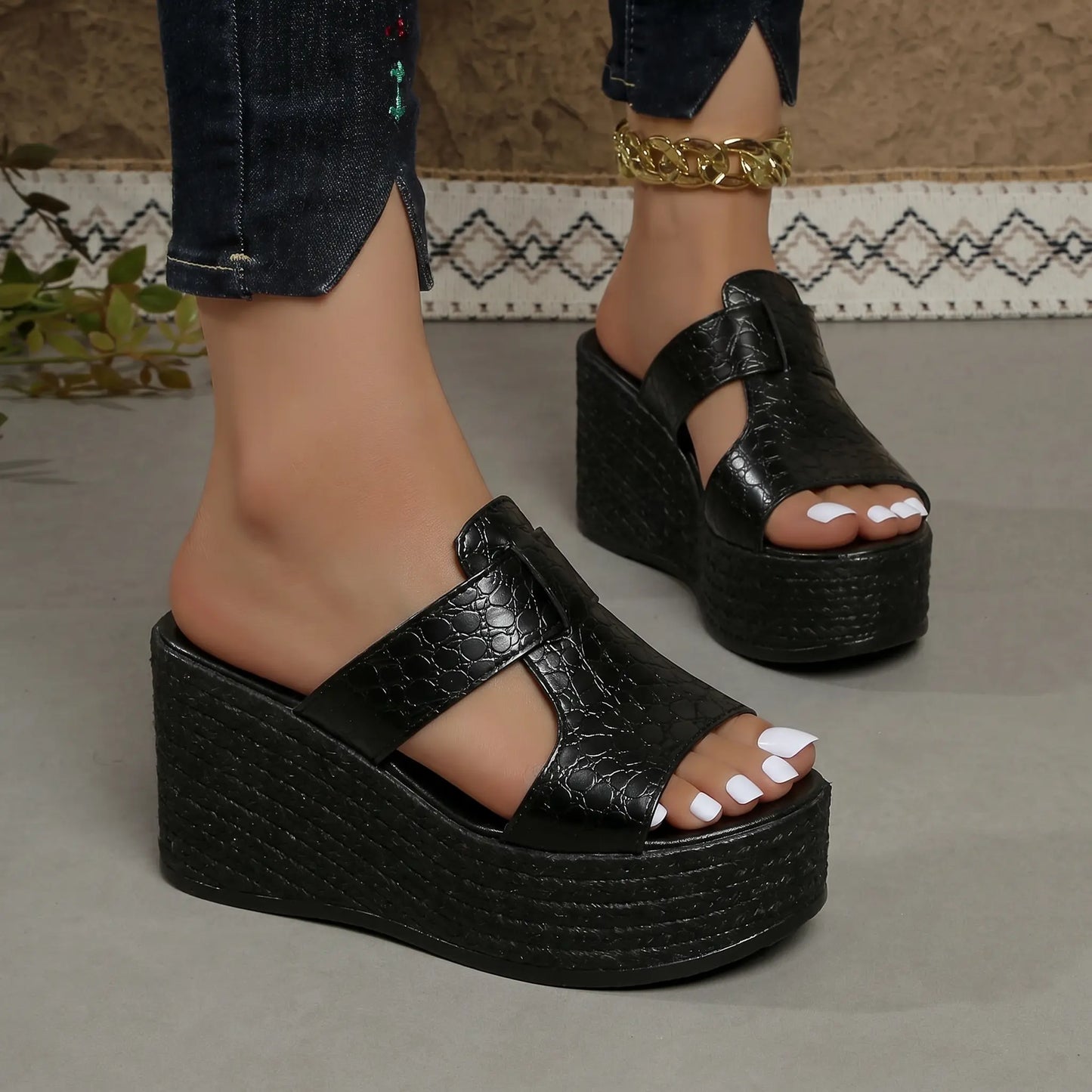 Black embossed PU leather Zylos platform wedge sandals with a textured finish, featuring a 4cm platform and 10cm wedge heel, shown on feet with white toenails and a gold anklet.