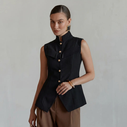 Elegant black sleeveless vest by Zylos, featuring a sharp mandarin collar, gold-tone button front, and a cinched waist with a flared peplum hem and split vent, worn by a model against a neutral studio background.