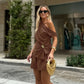 A woman models a chic chocolate brown linen-blend two-piece set featuring an asymmetrical draped top with a gold buckle accent and high-waisted shorts, styled outdoors.