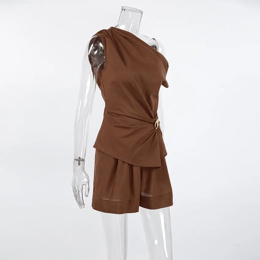 Aeloria chocolate brown linen-blend two-piece set featuring an asymmetrical draped top with a gold buckle accent and high-waisted shorts, shown on a mannequin.
