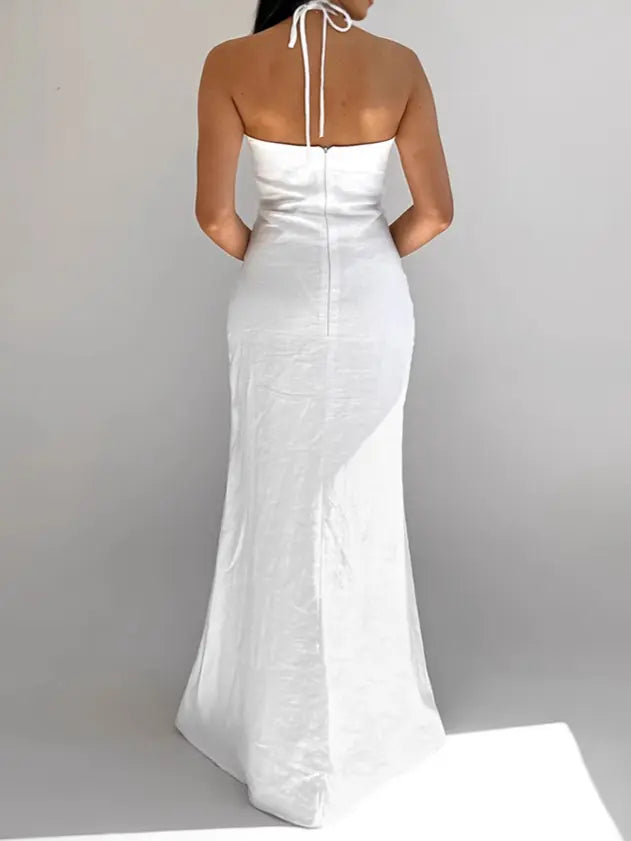 Back view of a white Aelyra halterneck maxi dress made from a textured cotton-linen blend, featuring a concealed zipper and flowing skirt. The thin straps tie at the nape of the neck.