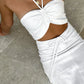 Close-up of a white Aelyra halterneck maxi dress featuring intricate ruching on the bust, a daring midriff cut-out, and an adjustable drawstring waist, styled with a delicate gold necklace.