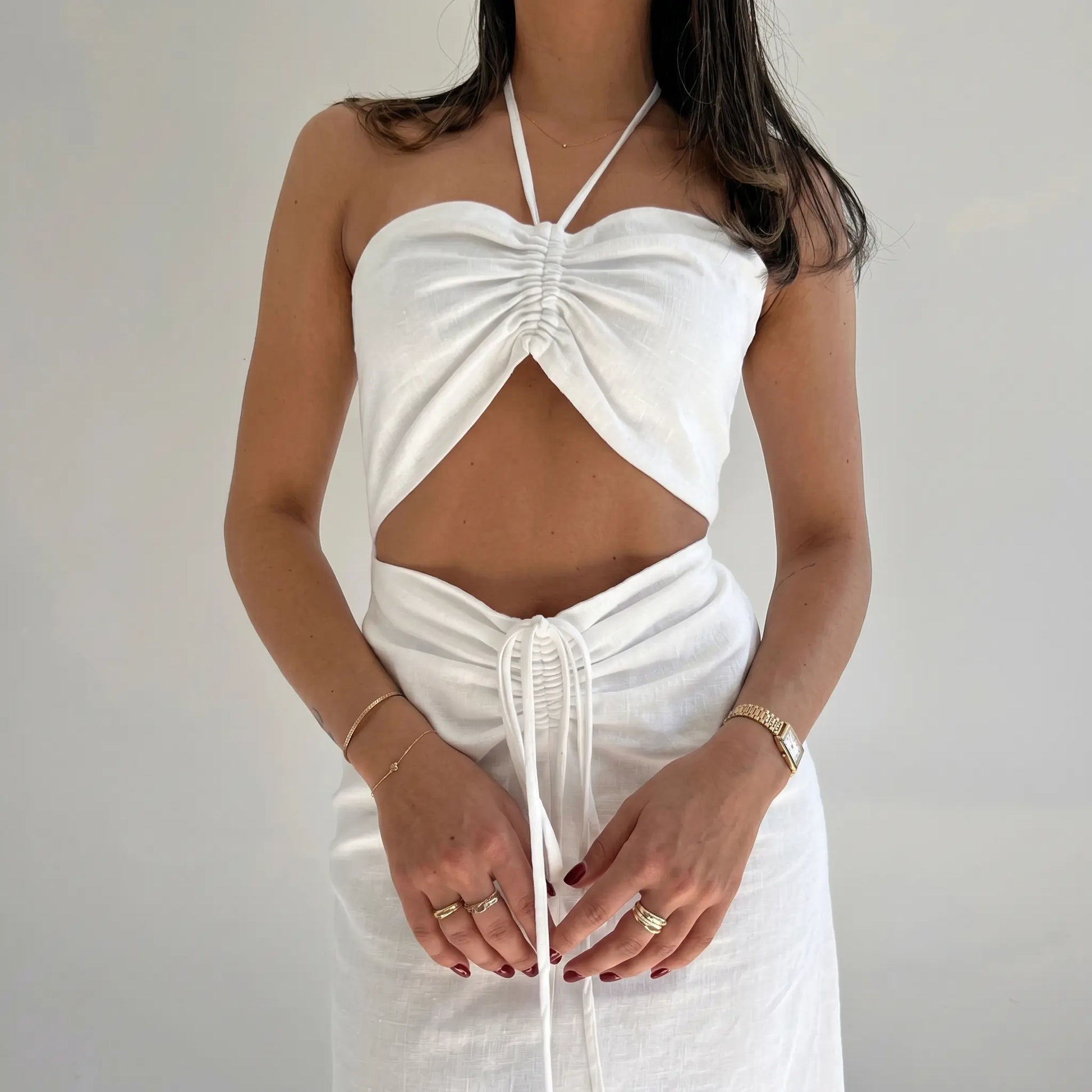 Aelyra white linen blend halterneck maxi dress with ruched bust, midriff cut-out, and drawstring waist, shown on a model from the front.