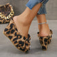 Woman's legs wearing leopard print wedge platform sandals with an oversized bow detail and peep-toe, paired with distressed denim jeans and a sparkling anklet.
