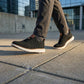 Aerostride Men's Breathable Knit Sneakers in black worn walking on a city street, showing the flexible mesh upper and white cushioned sole.