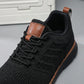 Aerostride men's breathable knit sneakers in black — close-up of engineered mesh upper, reinforced lacing, and brown vegan leather tongue patch.