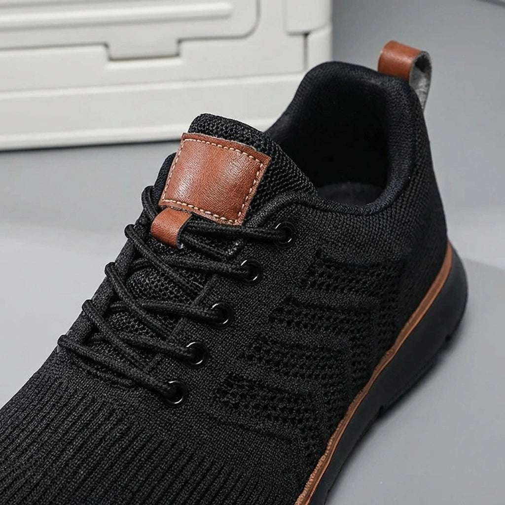Aerostride men's breathable knit sneakers in black — close-up of engineered mesh upper, reinforced lacing, and brown vegan leather tongue patch.