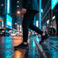 Aerostride Knit Urban Comfort sneakers in black worn on a wet city street, showing the side profile and anti-slip outsole traction.