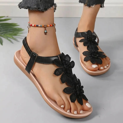 Black Aethel bohemian flat thong sandals embellished with layered floral appliques and a ribbed elastic slingback strap, shown on a model's foot.