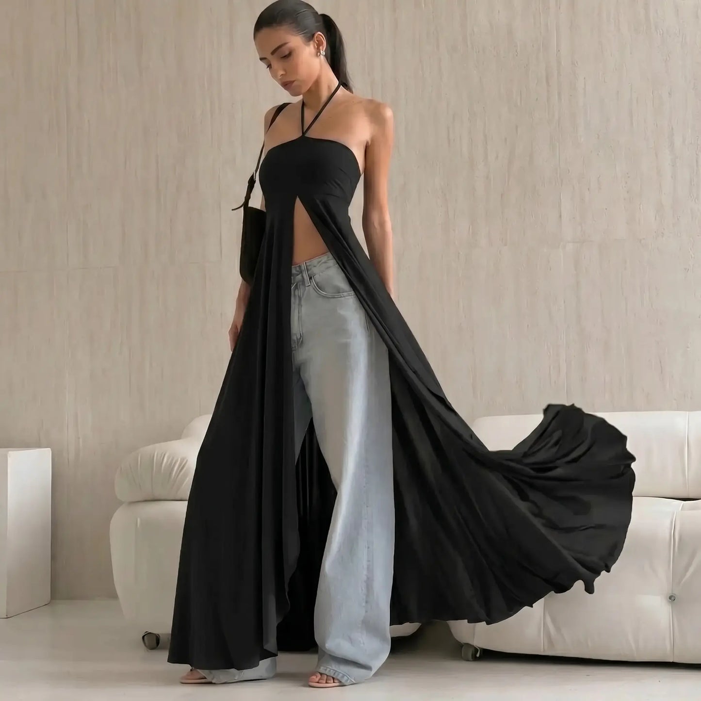 Black fluid halter maxi dress with a high front slit, styled over light-wash wide-leg jeans, showcasing a bohemian and romantic aesthetic. Full-length view.