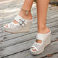 Cream Aethel woven wedge sandals with peep toe and dual buckle straps, elegantly worn on a wooden deck, showcasing their bohemian chic summer style.