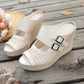 Cream Aethel woven wedge sandals with peep toe and dual buckle straps, displayed on a rustic wooden deck with a straw hat and flowers in the background.