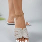A woman's feet wearing white Aethel crystal-embellished slide sandals with a square toe and flat sole, shown from the front on a studio background.