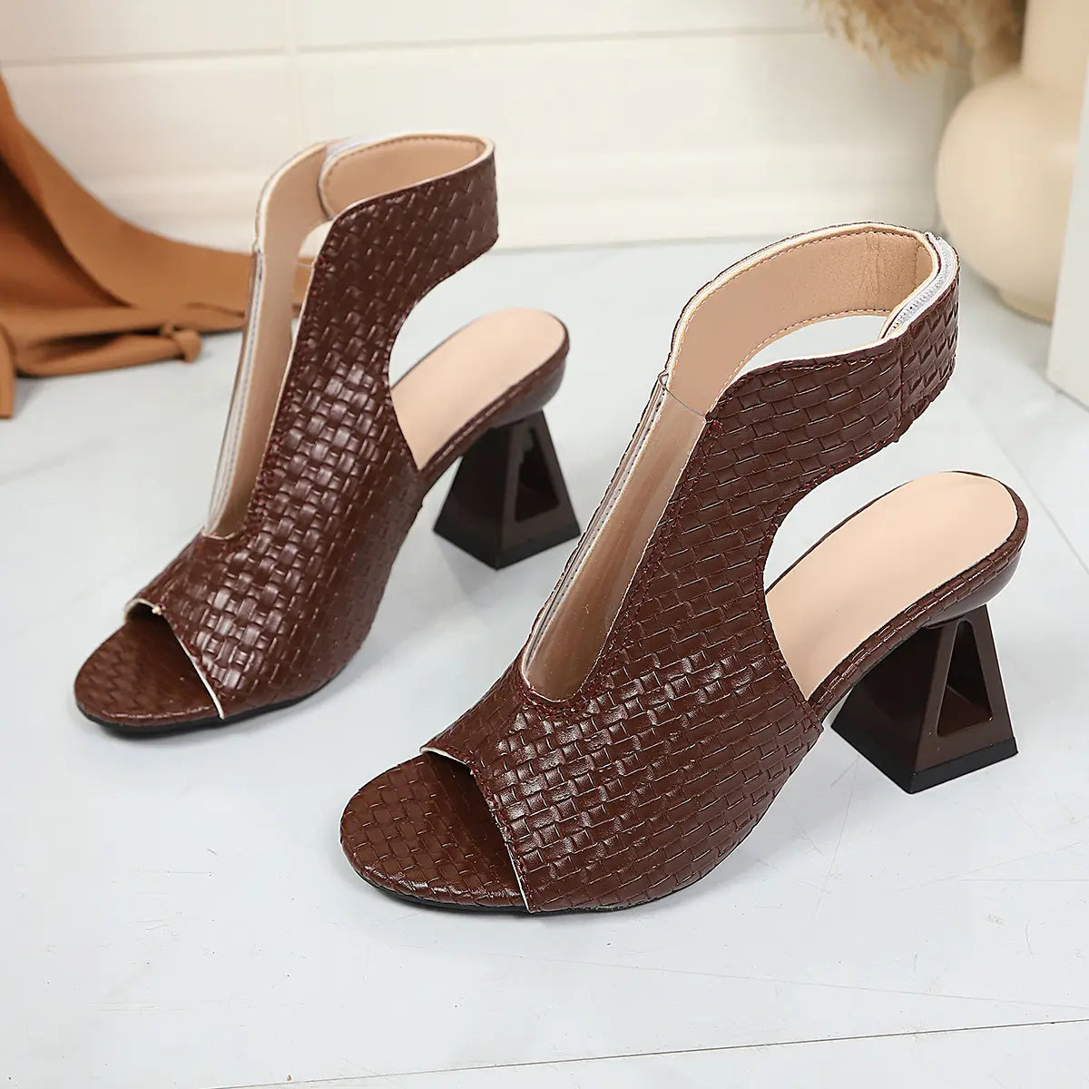 A pair of deep chestnut brown peep-toe block heel sandals with a distinctive woven texture and geometric heel, shown from a three-quarter angle.