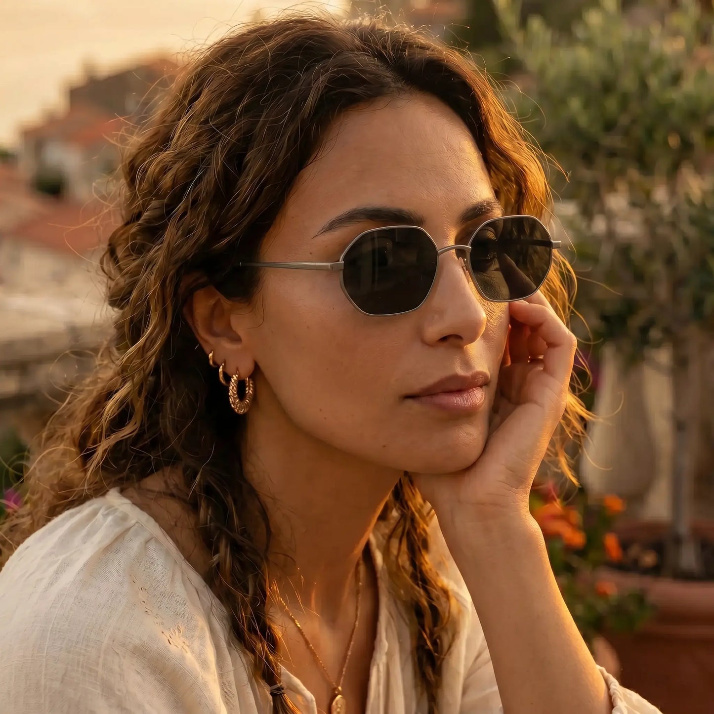 Woman wearing elegant octagonal gold-tone metal frame sunglasses with dark grey tinted lenses, styled outdoors in warm sunlight.