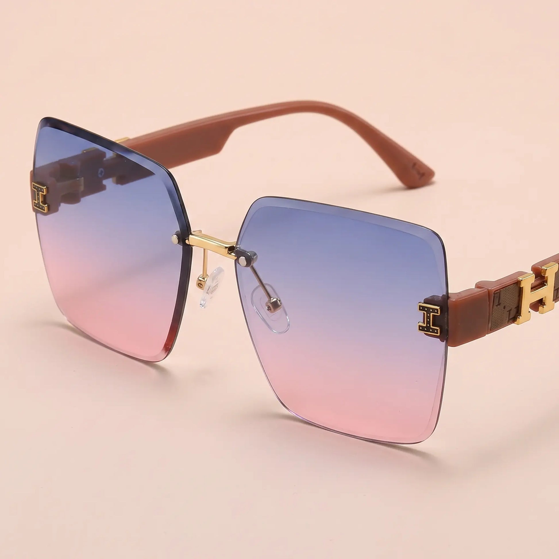 Aethel oversized square sunglasses featuring blue to pink gradient lenses and brown polycarbonate temples with gold-tone H logo accents. Three-quarter view.