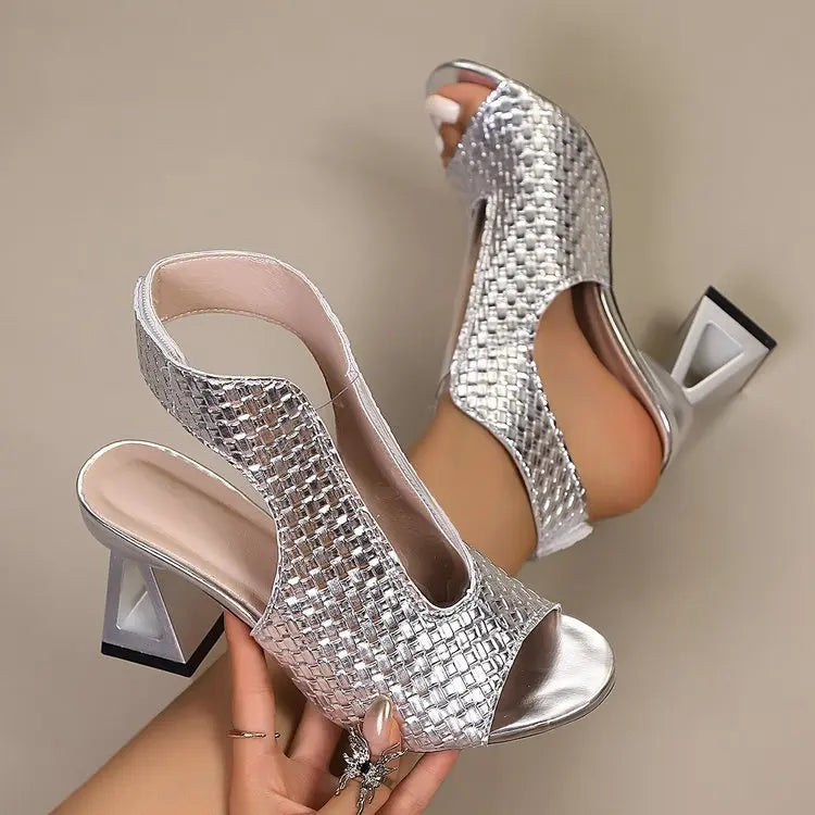 Silver Aethel peep-toe block heel sandals with intricate woven detail and a metallic chain ankle strap shown from a three-quarter angle.