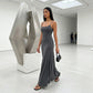 Aethel sleek maxi dress in charcoal grey with spaghetti straps, worn by a model walking in a modern art gallery.