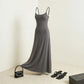 Aethel sleek maxi dress in charcoal grey with adjustable straps, styled with a black handbag and strappy sandals in a studio setting.